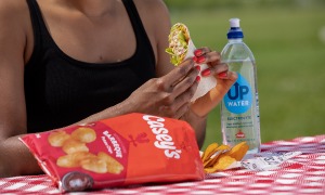 A woman eating Casey's chips, a wrap, and water at a picnic table