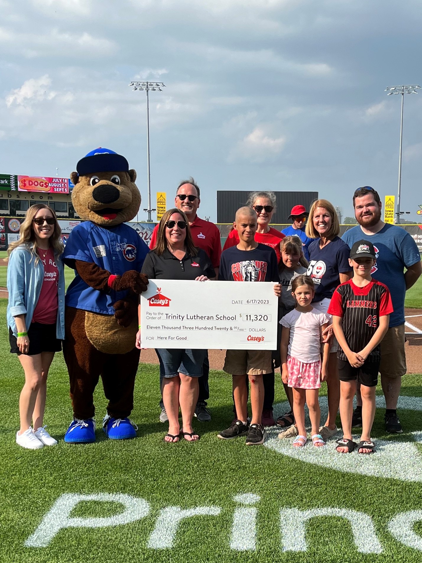 Trinity Lutheran School representatives holding a giant check at Principal Park baseball field.