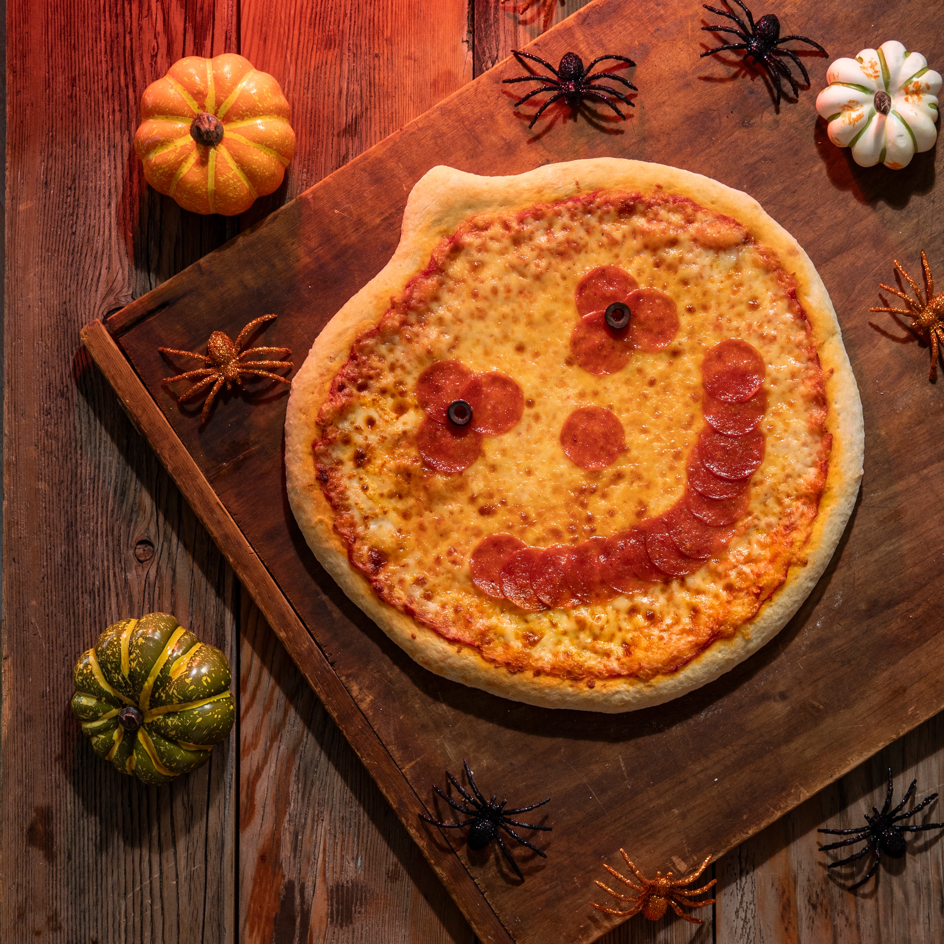 A Jack-O'-Lantern Halloween Pizza on a table with mini pumpkins and spiders
