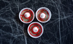 Eyeball Jell-O Shots with red food coloring on a spiderweb spooky background