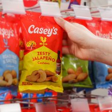 Someone grabbing a bag of Casey's Zesty Jalapeno Cashews made from Lola's Hot Sauce