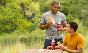 Two men enjoying subs and Cokes on a picnic table