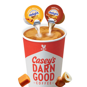 Cup of hot coffee with hazelnut and caramel macchiato creamer being poured in.