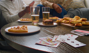 Friends sitting around a table playing cards, drinking beer, and eating Casey's pizza and breadsticks