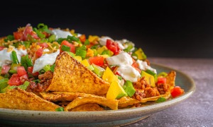 A plate of loaded Nachos with cheese, veggies, sour cream, and more