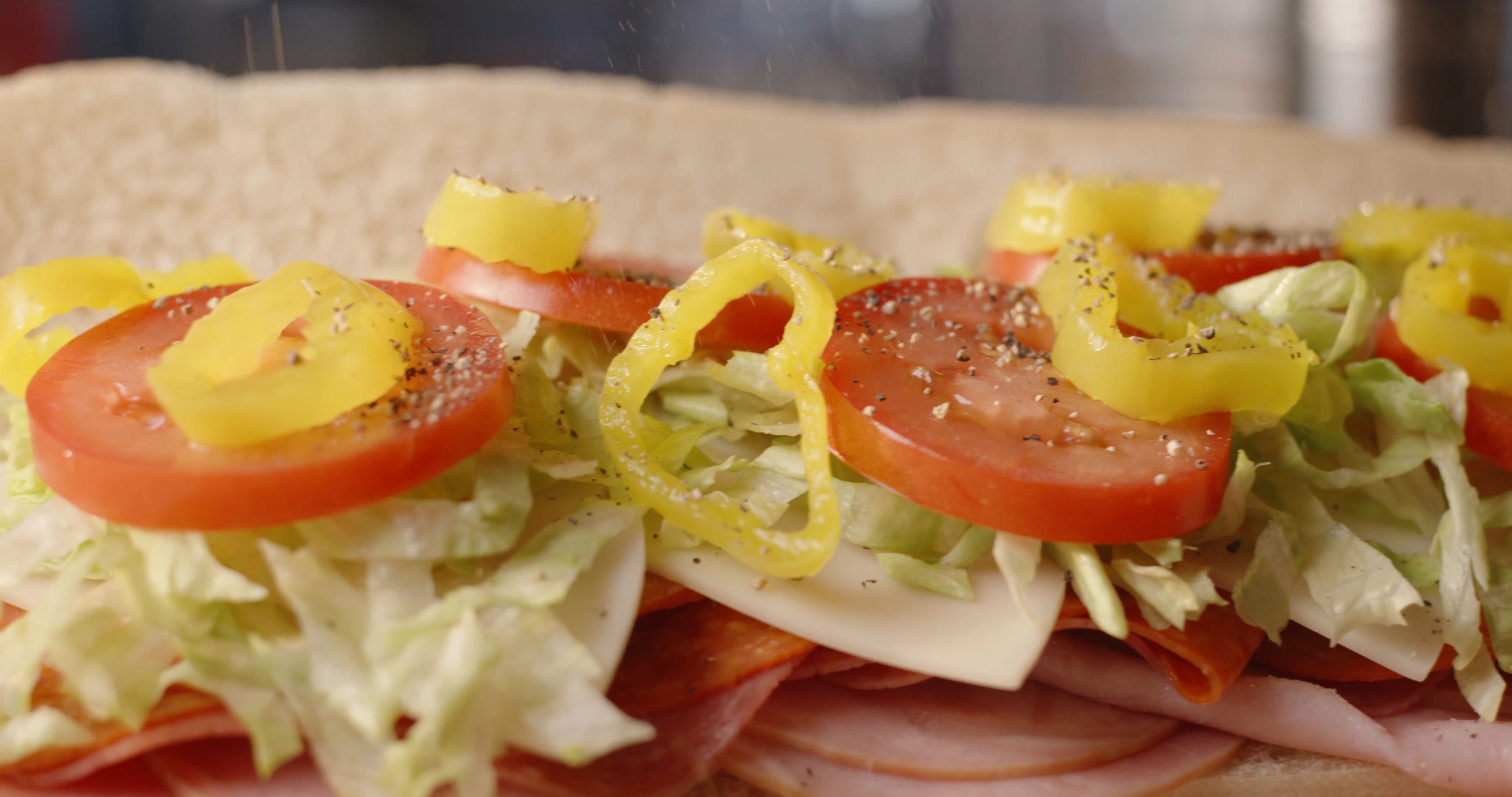 A close up of fresh tomatoes, banana peppers, lettuce, meats, and cheeses on a Casey's sub sandwich