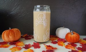A Halloween glass filled with a Hot Pumpkin Cocktail by some decorative pumpkins and leaves