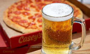 A glass of beer in front of a Casey's Pepperoni Pizza