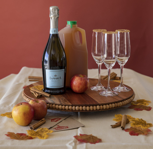 Three Apple Cider Mimosas with apples, cinnamon sticks, champagne, and fall leaves